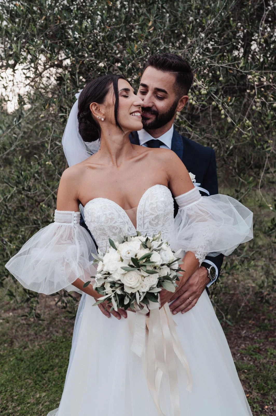 Gli sposi abbracciati tra gli alberi, con il bouquet in primo piano.
