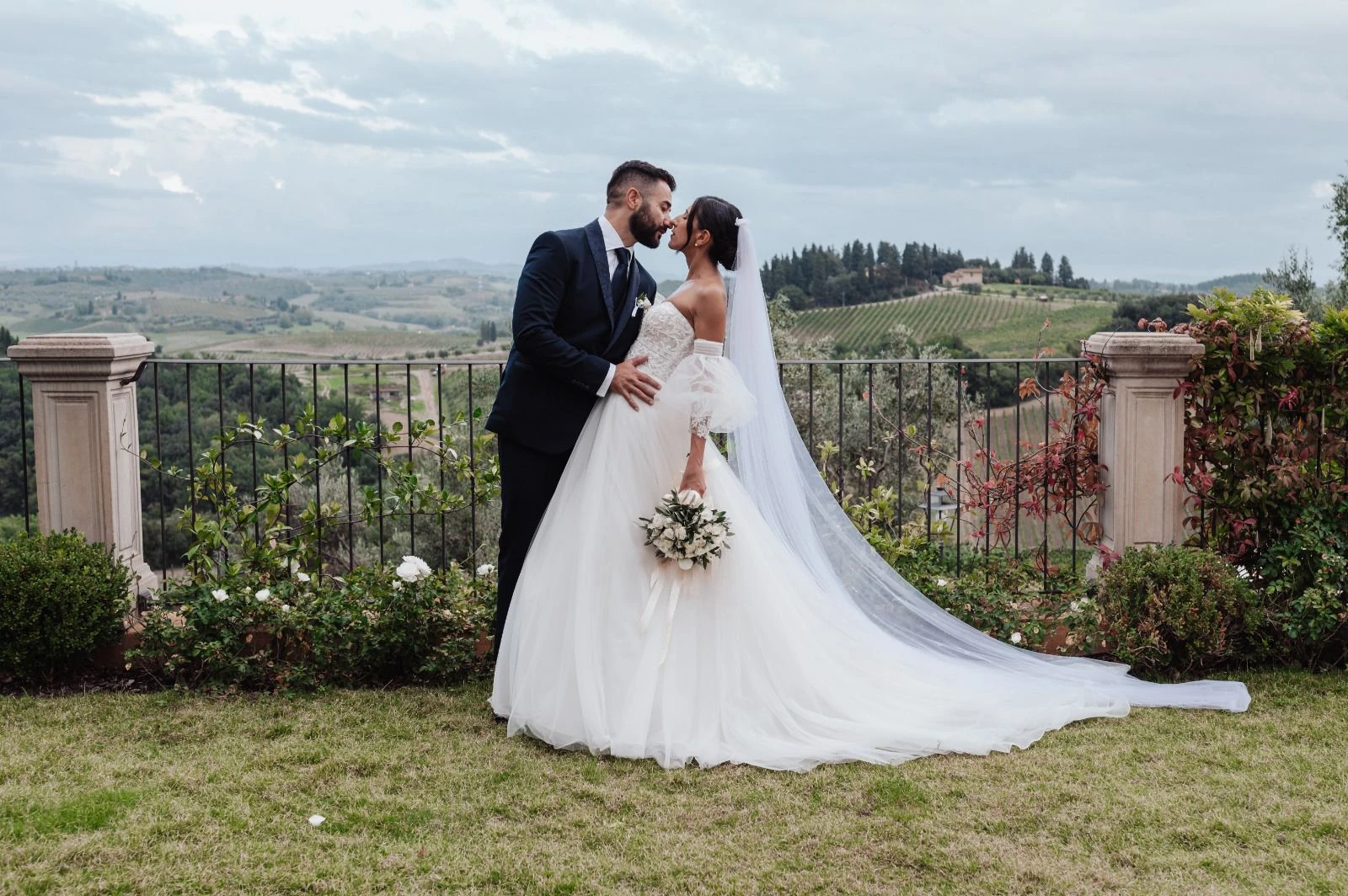 Gli sposi si baciano in un giardino affacciato sulle colline.