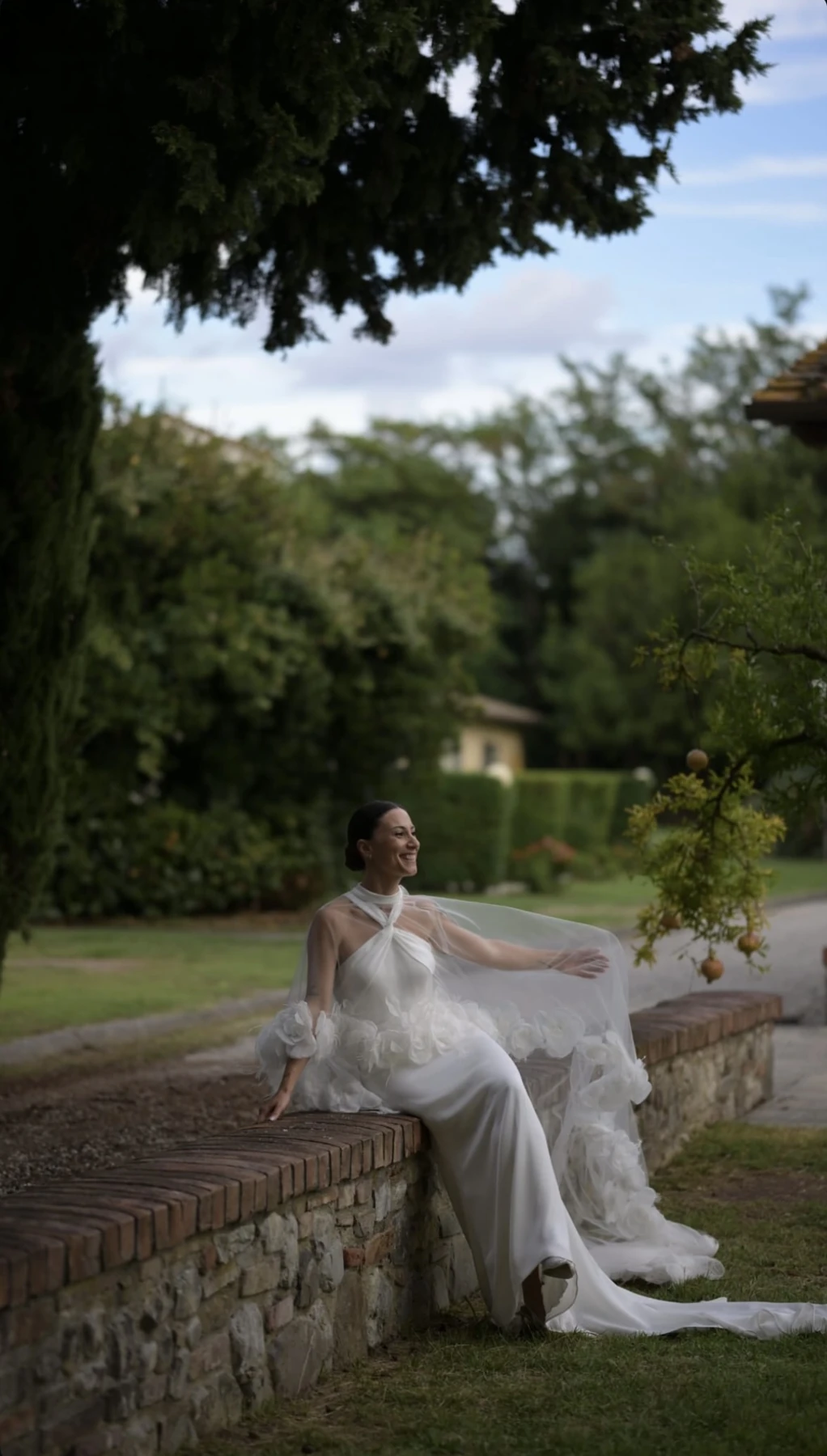 Sposa seduta su un muretto in giardino.