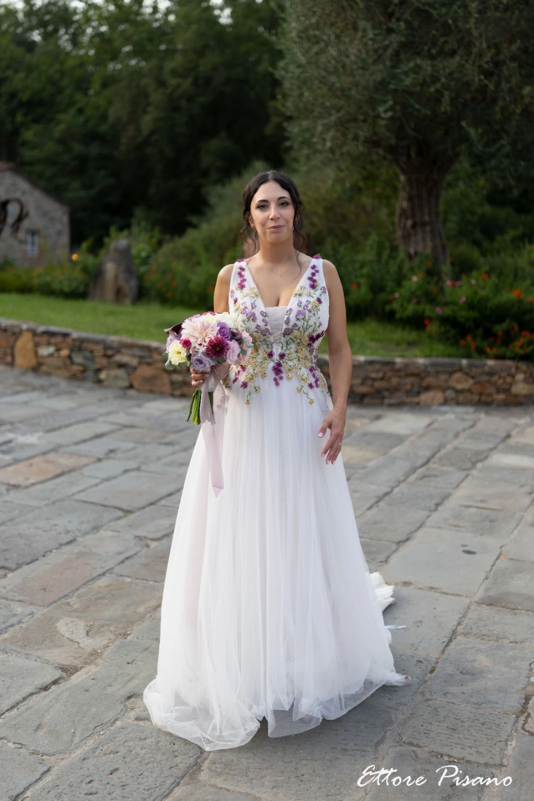 Sposa con bouquet su un percorso pavimentato in giardino.