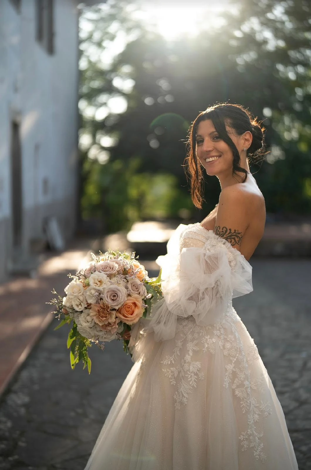 Sposa con bouquet e abito con maniche morbide, ritratta all'aperto in controluce.