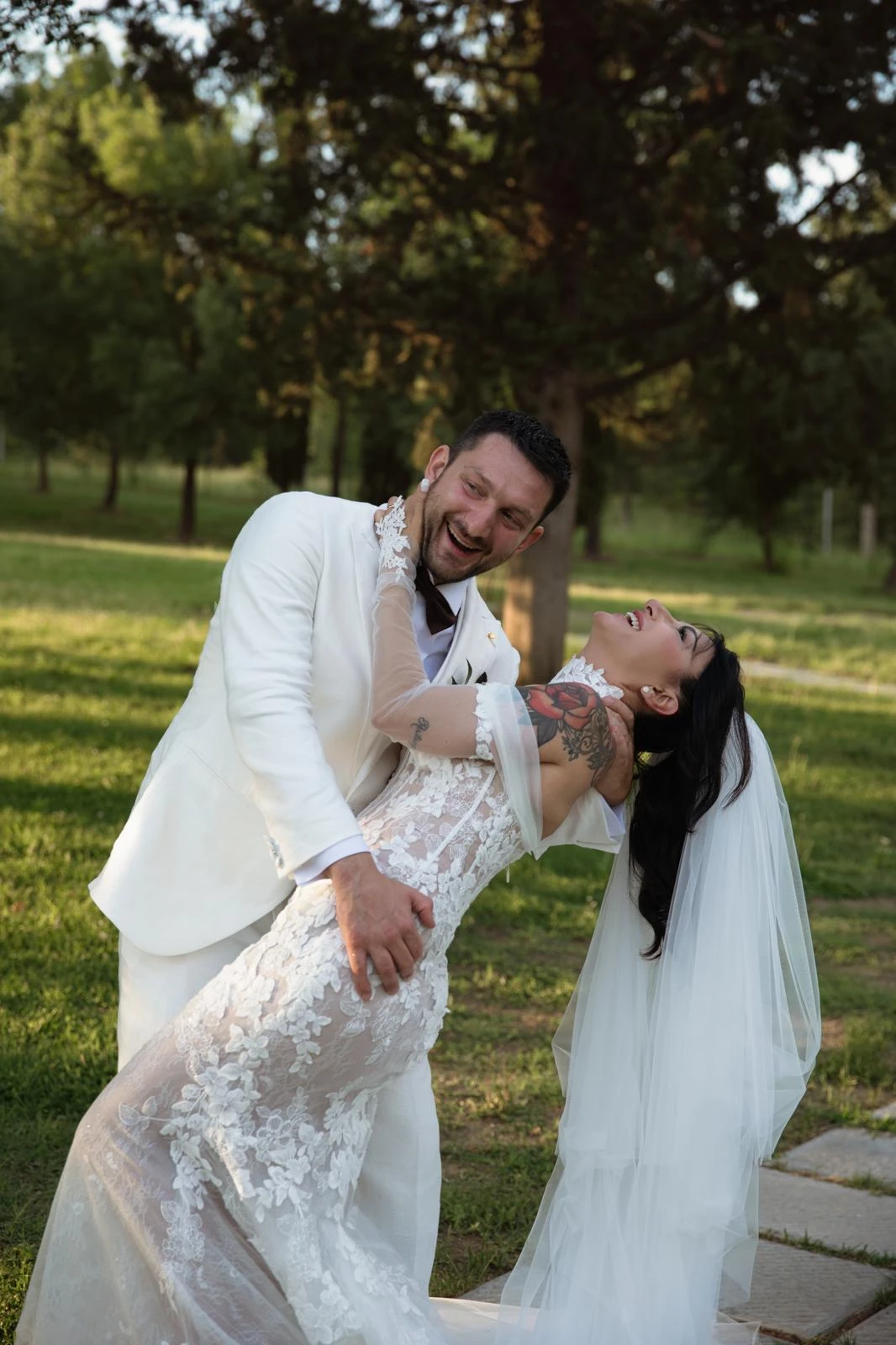 Lo sposo in abito chiaro abbraccia la sposa inclinata tra le sue braccia in giardino.