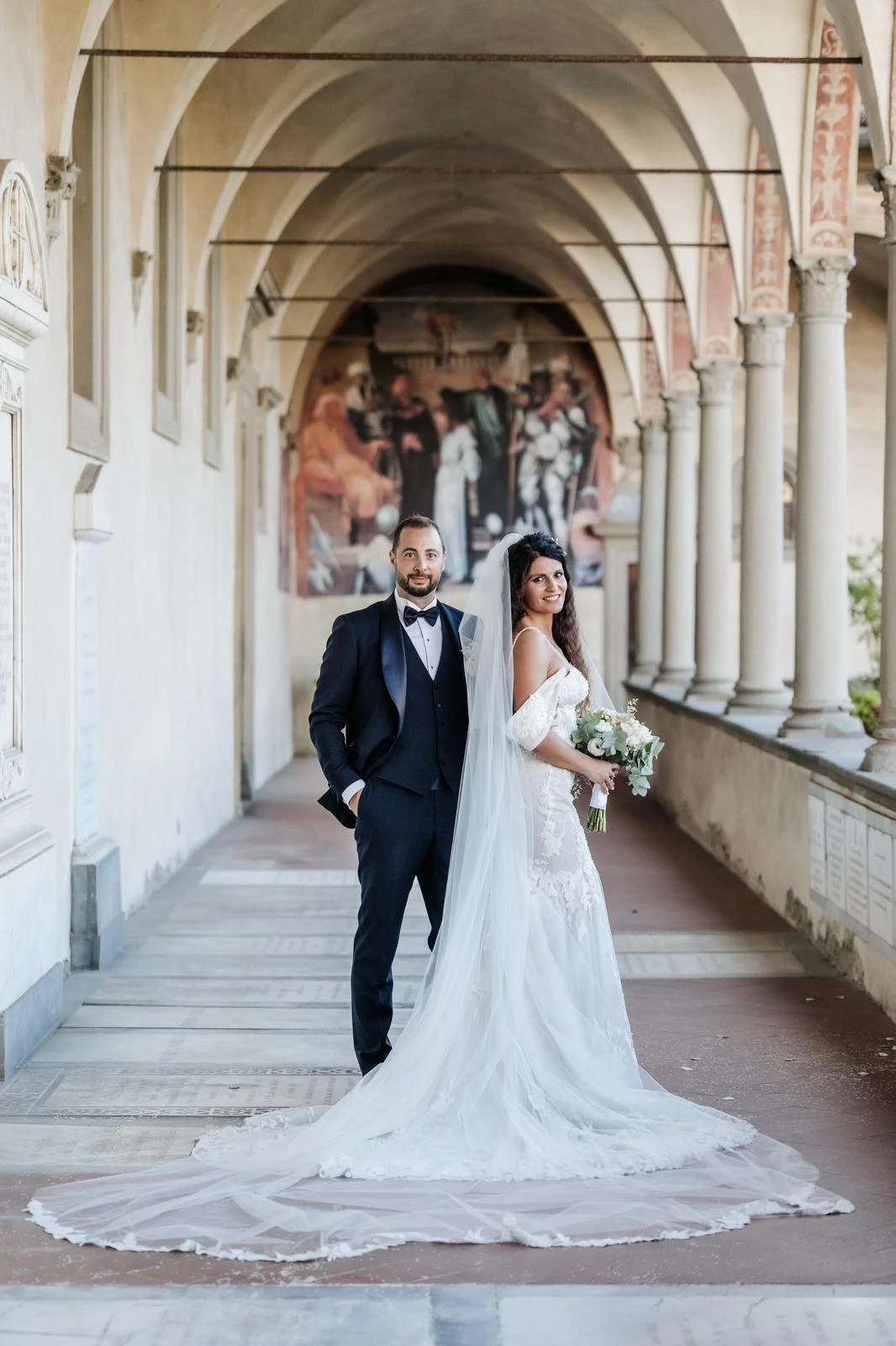 Gli sposi sotto un porticato, con lo strascico della sposa disteso davanti a loro.
