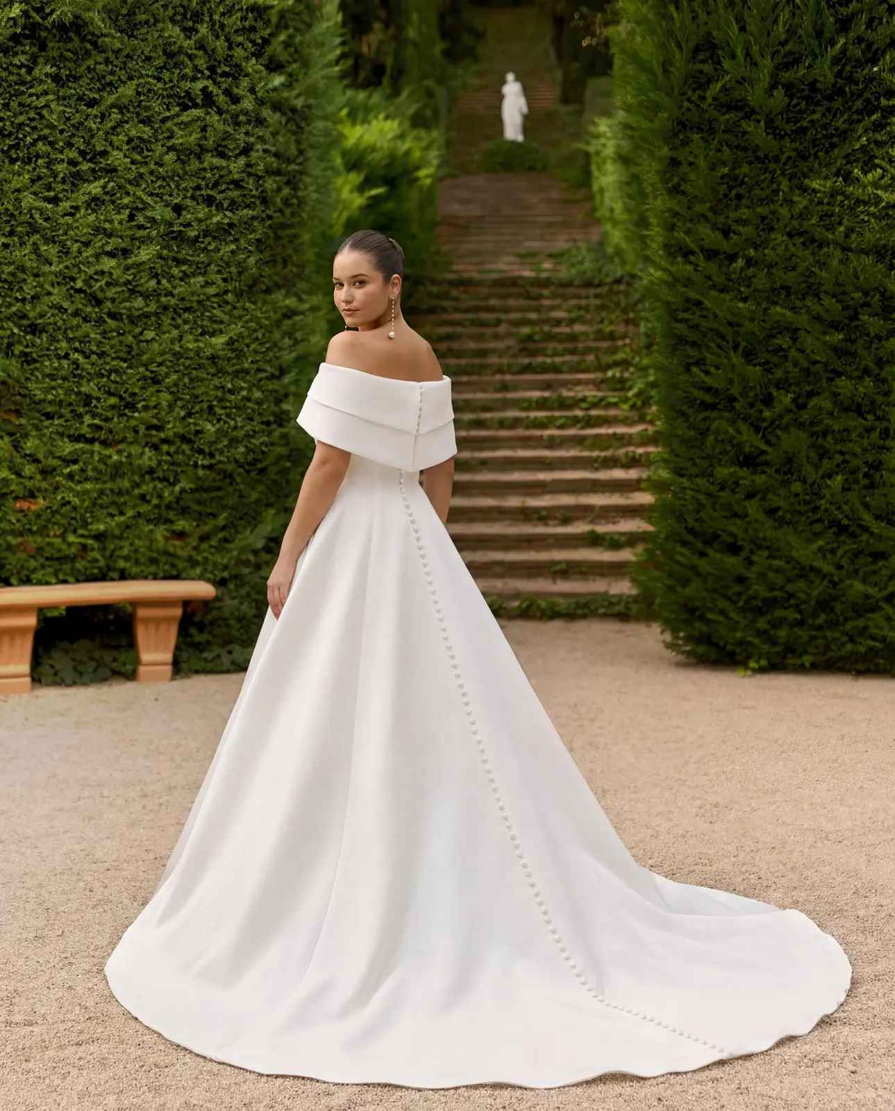 Vista posteriore di un abito da sposa con fascia sulle spalle, fila di bottoni e ampio strascico.
