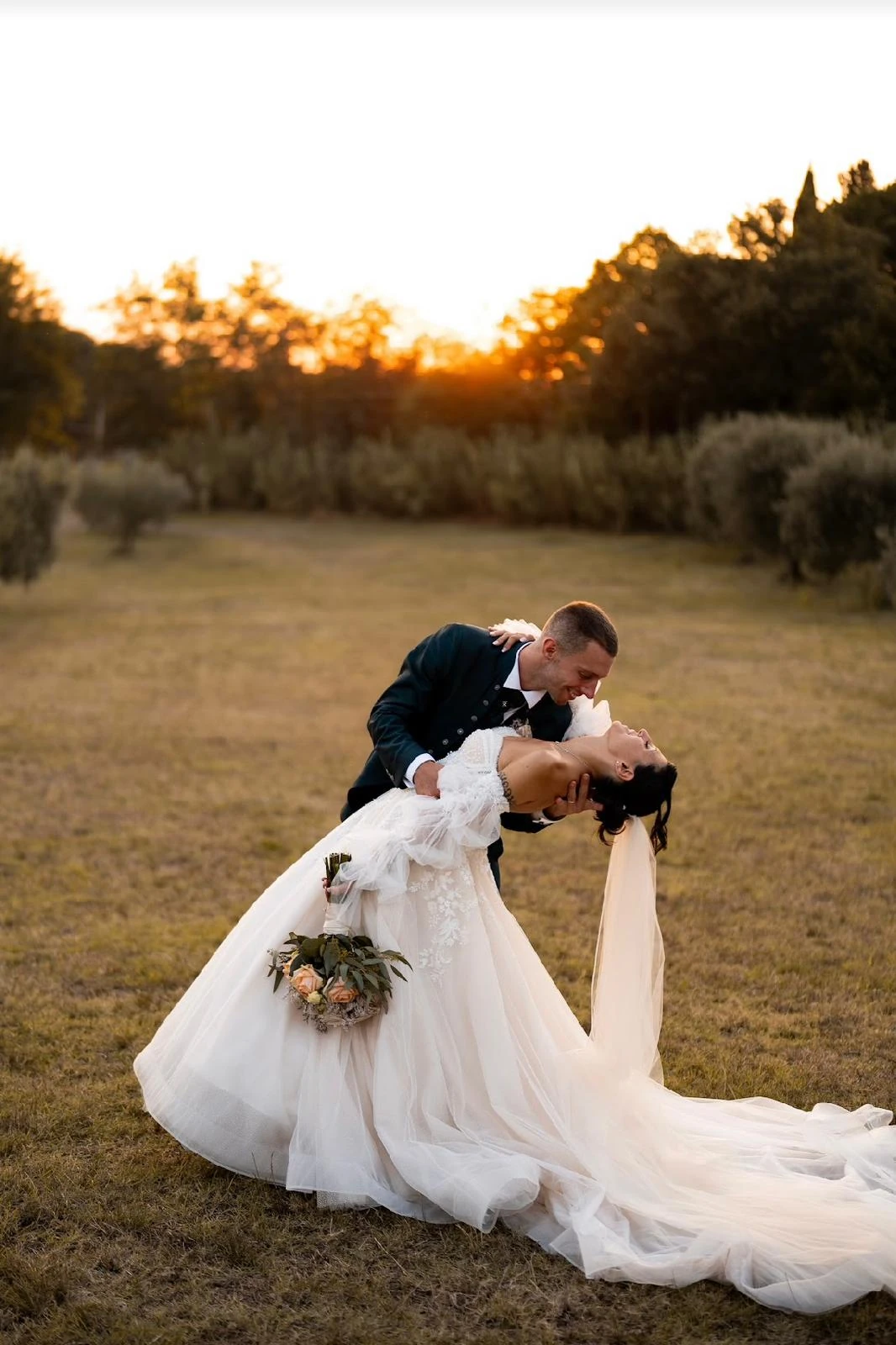 Gli sposi si baciano con la sposa inclinata tra le braccia dello sposo, su un prato.