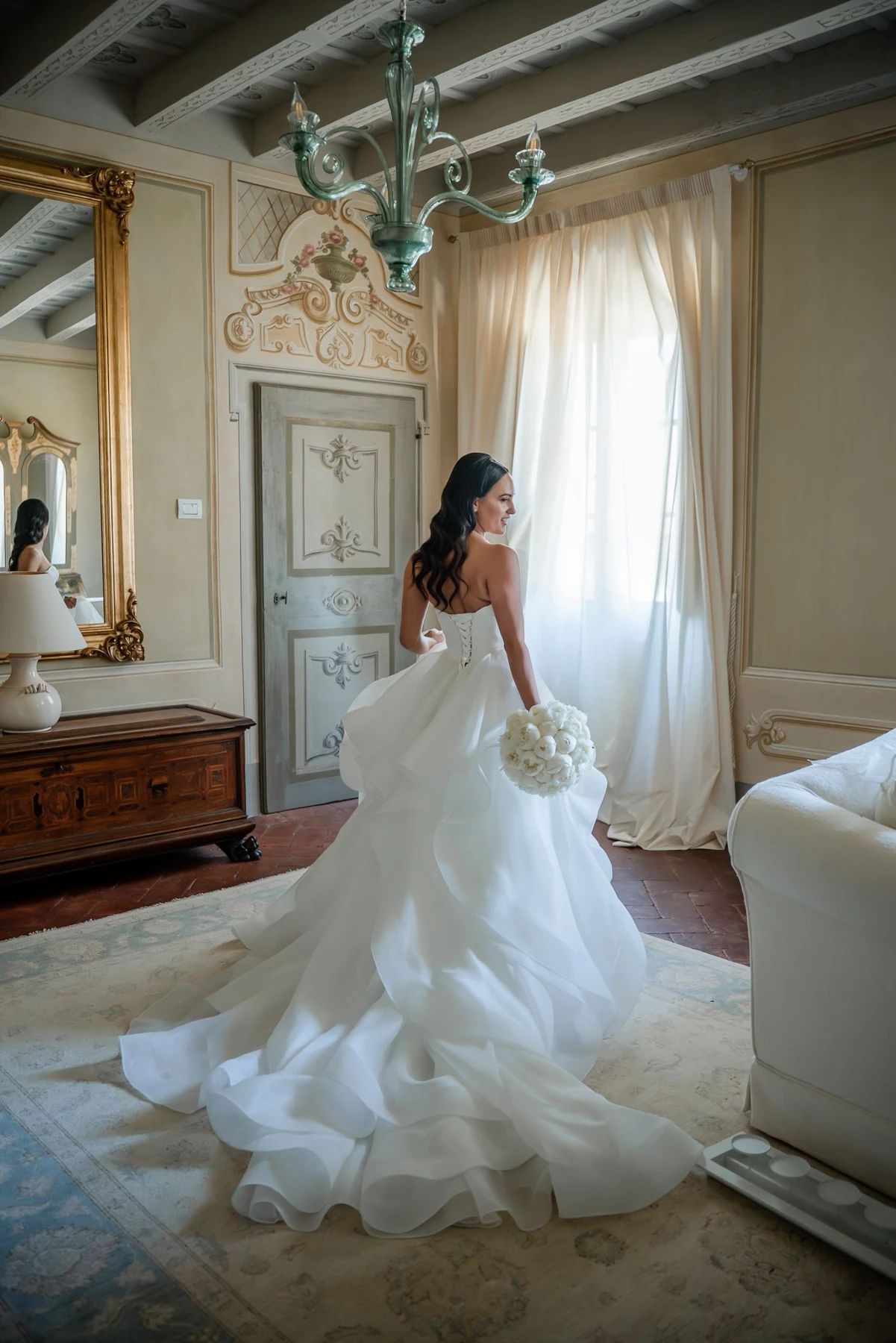 Sposa vista di spalle in una stanza, con lo strascico disteso sul pavimento.