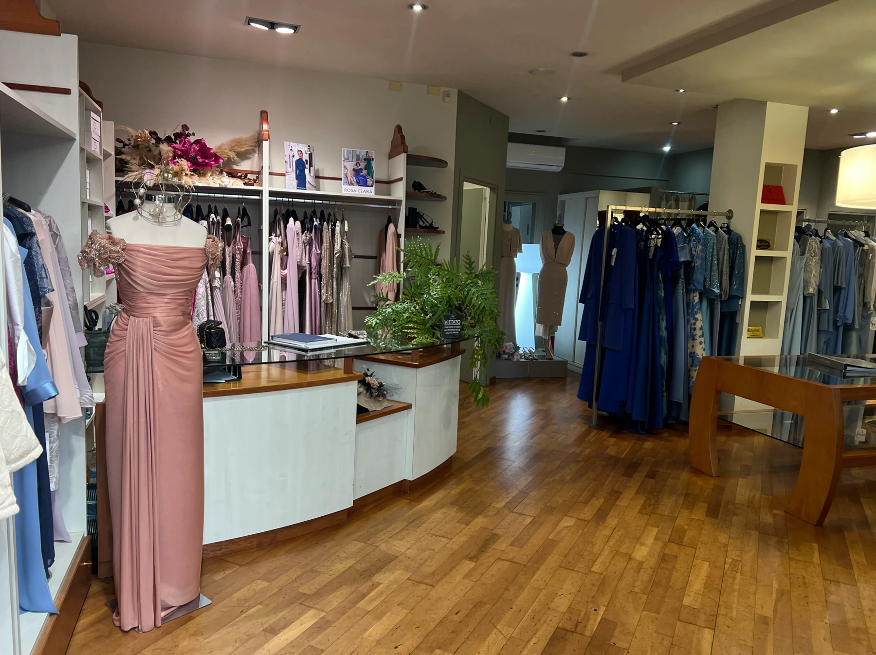 Interno della boutique con banco, abito rosa e abiti esposti.